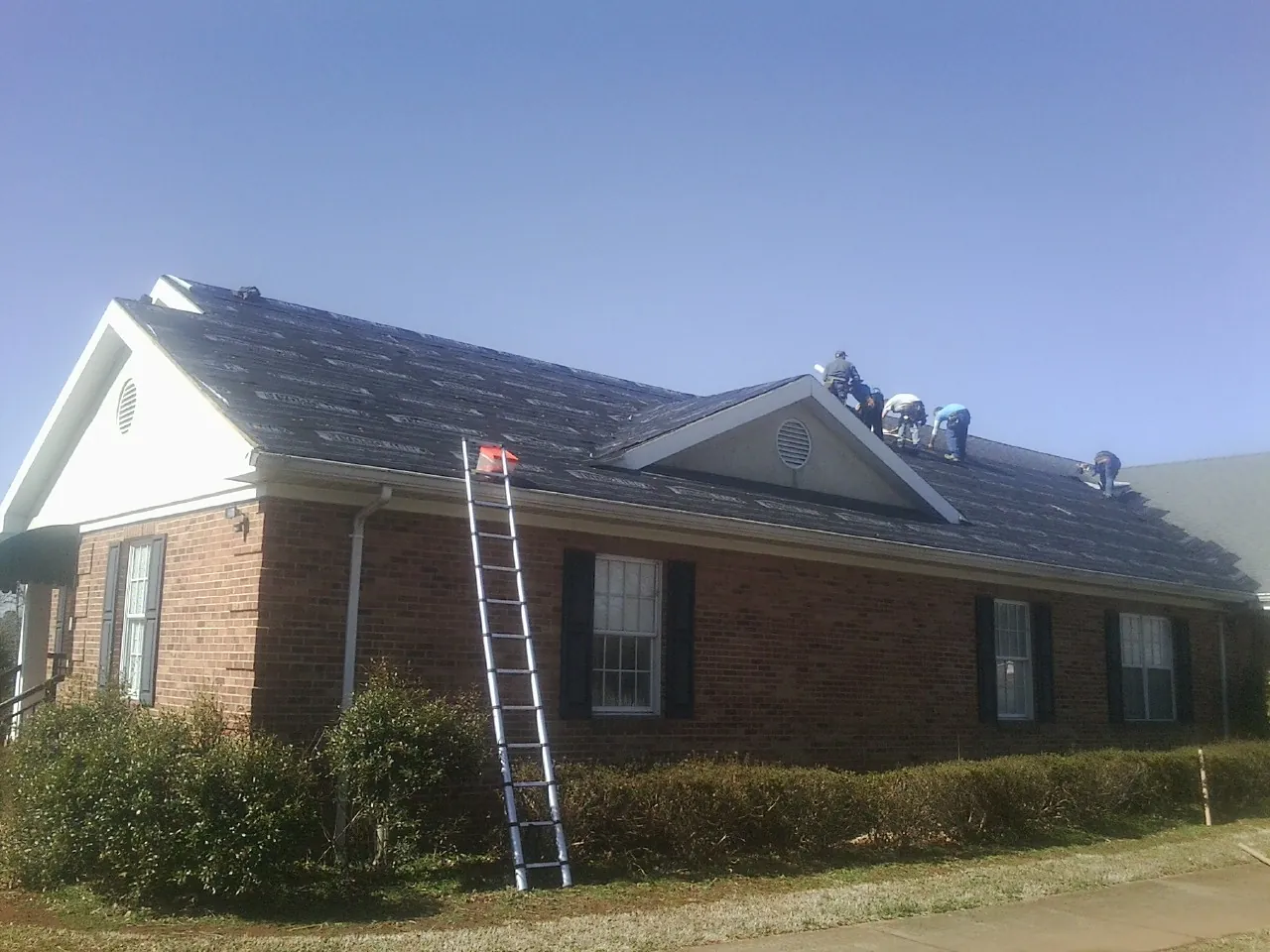 Crew tearing shingles off a brick ranch roof with a ladder set — Metal Roof Repair work by our crew in Emmett
